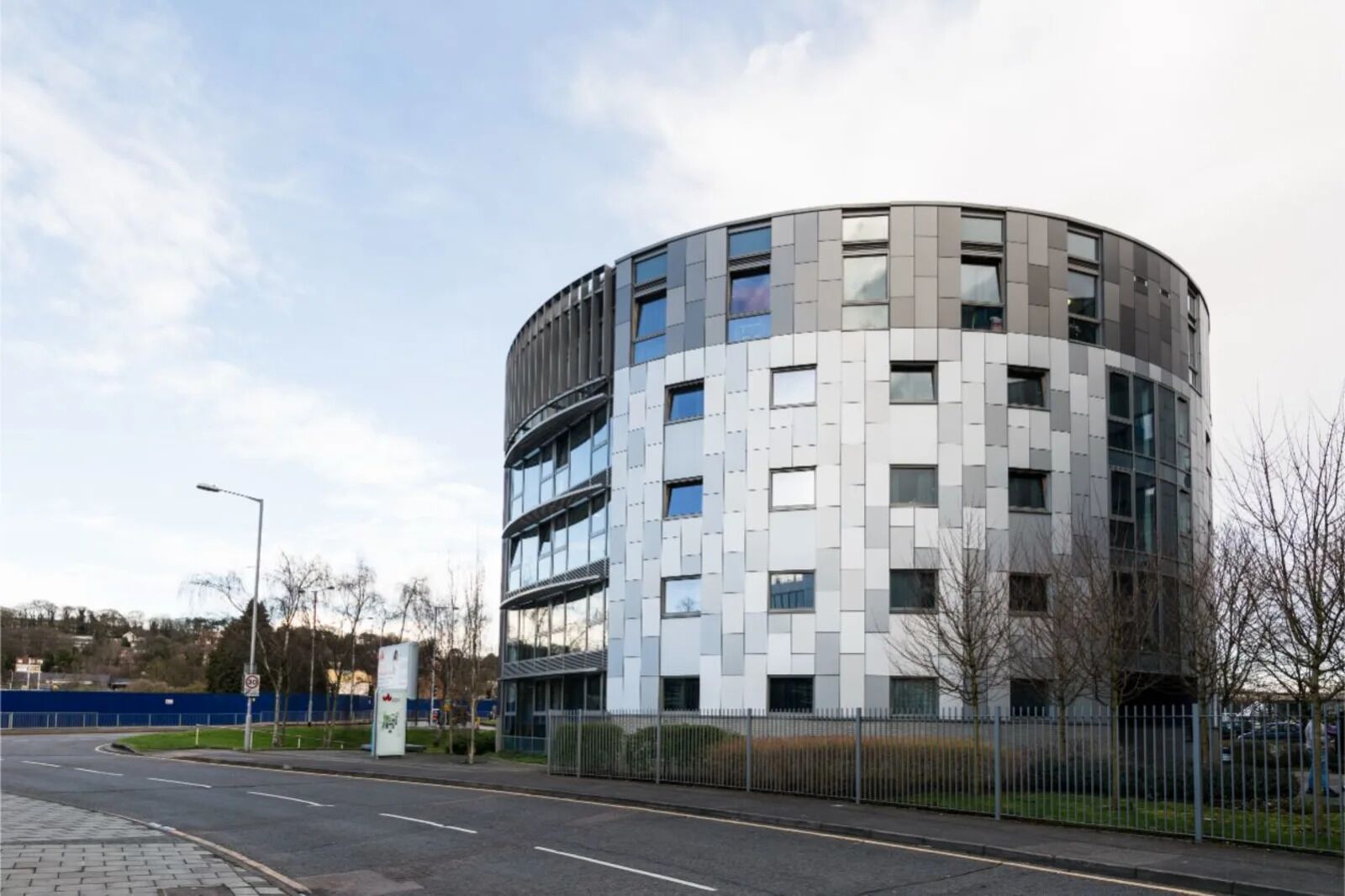 A modern, multi-story building with a curved facade, large windows, and a gated entrance.