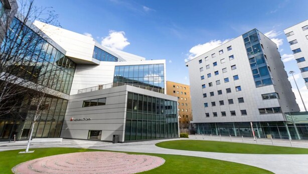 Ein moderner Gebäudekomplex mit Glasfassaden, einem zentralen Innenhof im Kreisdesign und angrenzenden Wohngebäuden.