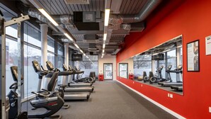 Ein Fitnessstudio mit Laufbändern und Trainingsgeräten, großen Fenstern und einer roten Akzentwand.
