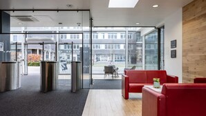 Eine moderne Lobby mit Glastür, roten Sitzgelegenheiten und einer Wandvertäfelung aus Holz.