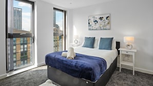 Una habitación de hotel moderna con una cama grande, una mesita de noche con lámpara y un cuadro en la pared.