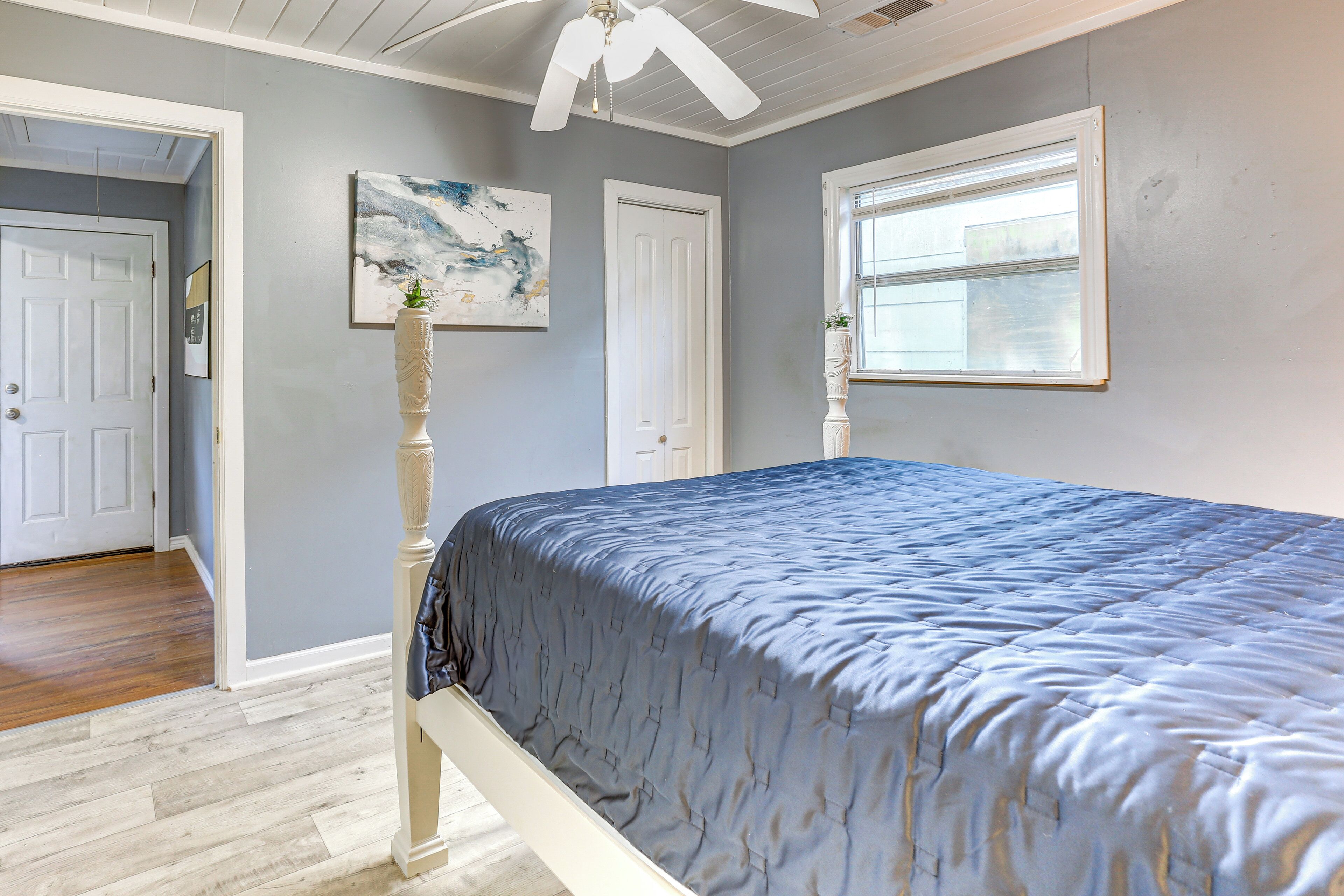 Une chambre à coucher avec un lit, un ventilateur de plafond, une fenêtre et une porte.