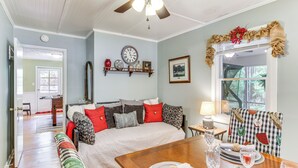 Una habitación acogedora con cama, una mesa de comedor con vasos y platos, un reloj en la pared y una ventana con vistas a árboles.