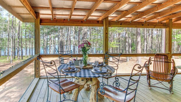 Un área de comedor al aire libre y cubierta con una mesa y sillas de madera, rodeada por un bosque.