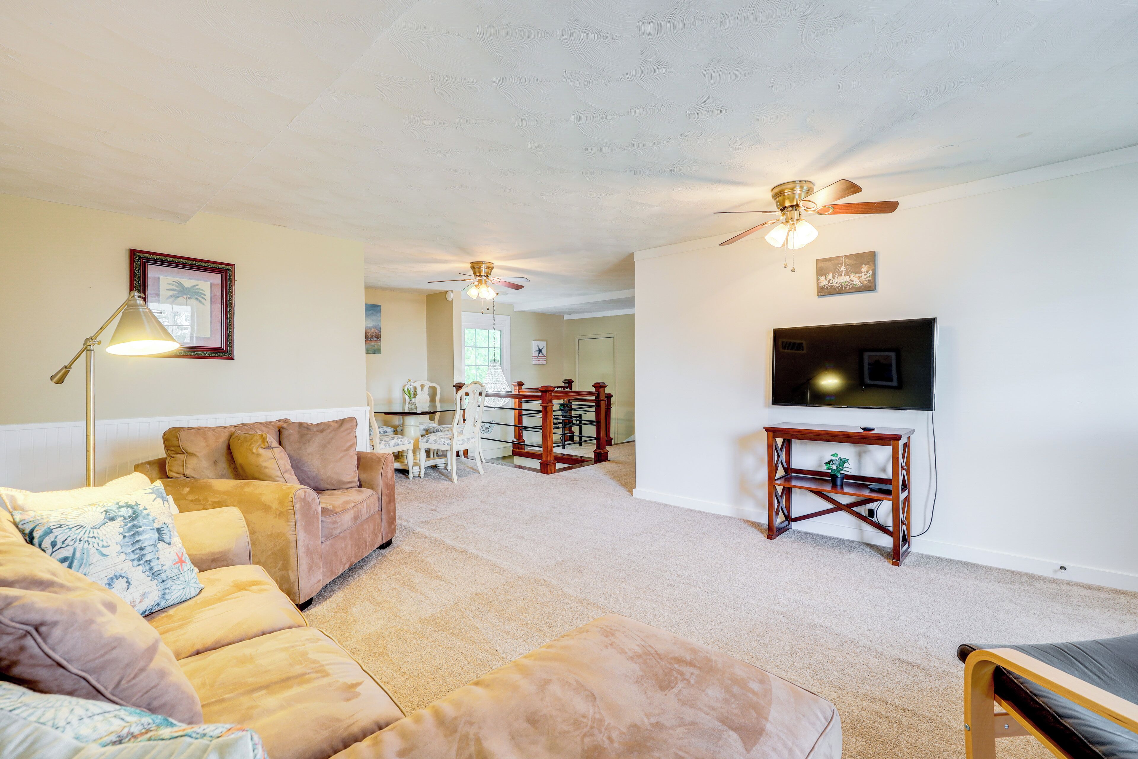 A living room with a beige carpet, a brown leather sofa, a wooden coffee table, and a ceiling fan.