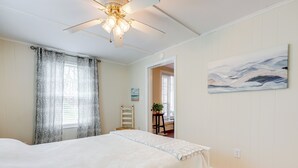 A bedroom with a bed, a ceiling fan, a painting, and a window with patterned curtains. - St. Marys Chic: Porch Living & Total Walkability! (St. Marys)