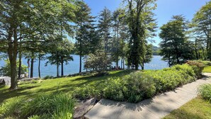 A lakeside garden with a concrete path, lush greenery, and a view of the lake.