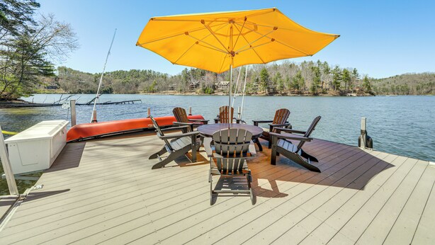 A wooden deck with outdoor furniture, including chairs and a table, overlooking a body of water.