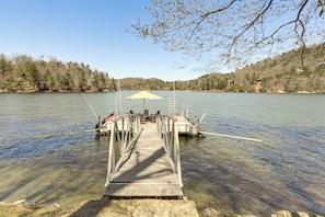 Une jetée en bois s’avance sur un lac, et à son extrémité, on aperçoit un parasol jaune et des chaises.