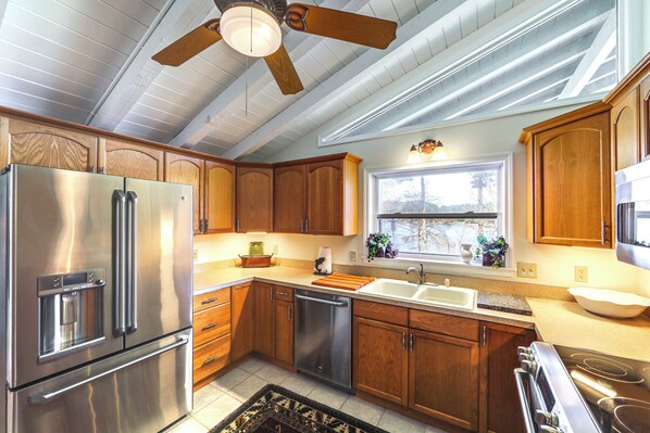 A kitchen with wooden cabinets, stainless steel appliances, a dishwasher, and a window with a view. - Mtn-view Home on Lake Glenville w/ Dock (Cashiers)