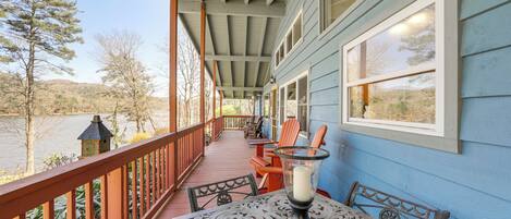A covered porch with a table and chairs, overlooking a body of water and hills.