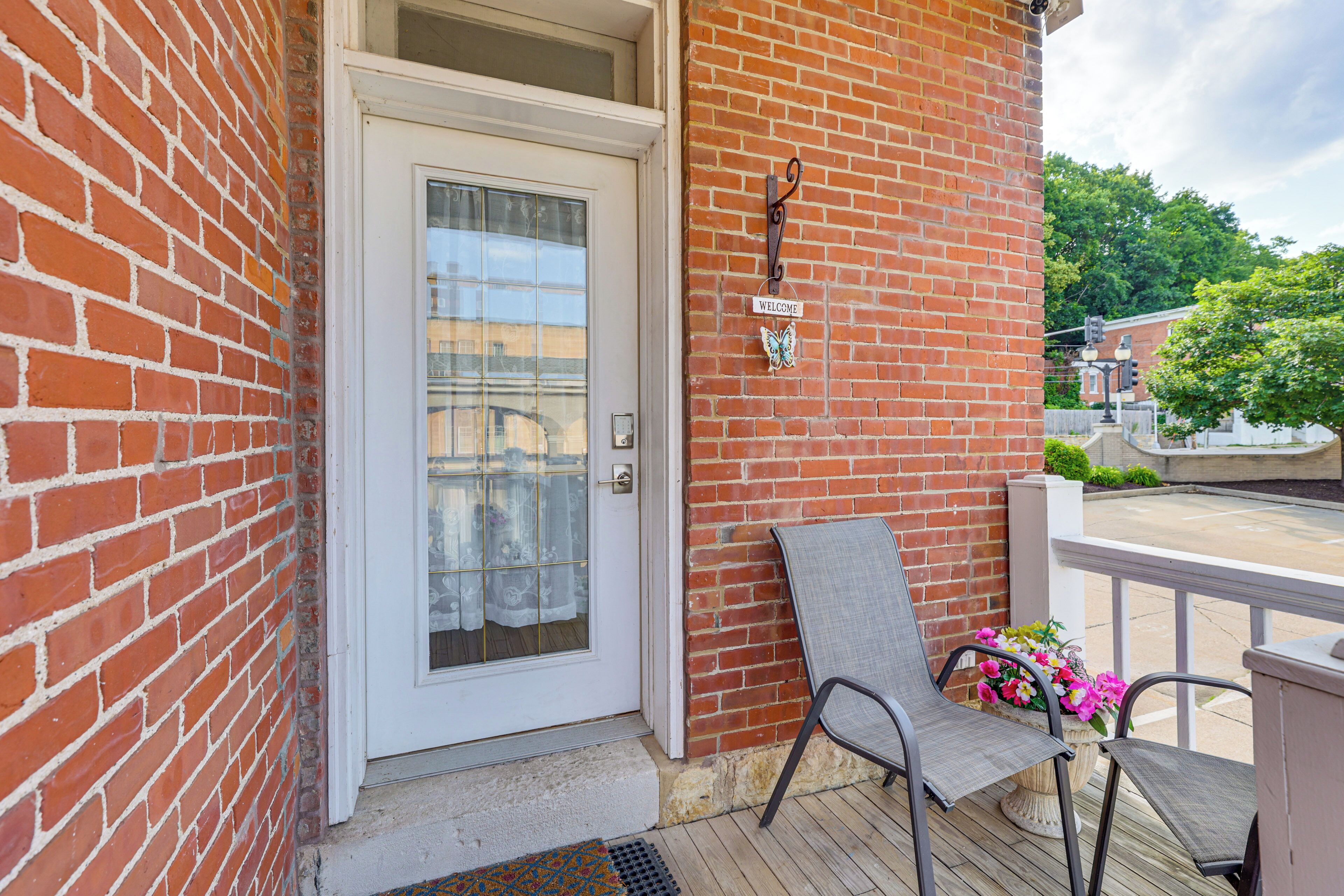 A brick building with a white door, a welcome sign, and a chair on a wooden deck.