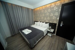 Habitación de hotel con cama, mesita de noche y cortina.