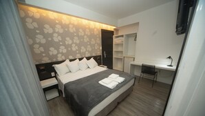 A modern hotel room with a bed, bedside tables, a desk, and a chair.