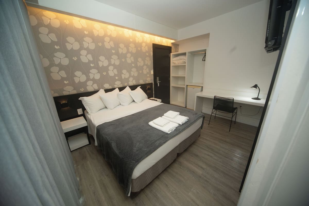 Quarto de hotel moderno com cama, mesas de cabeceira, escrivaninha e uma cadeira.