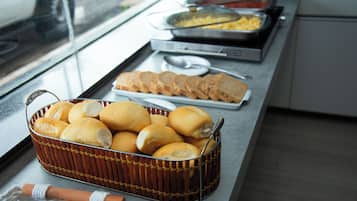 Una mesa de buffet con diversos alimentos, incluyendo panes, un cesto de panecillos y una bandeja de huevos revueltos.