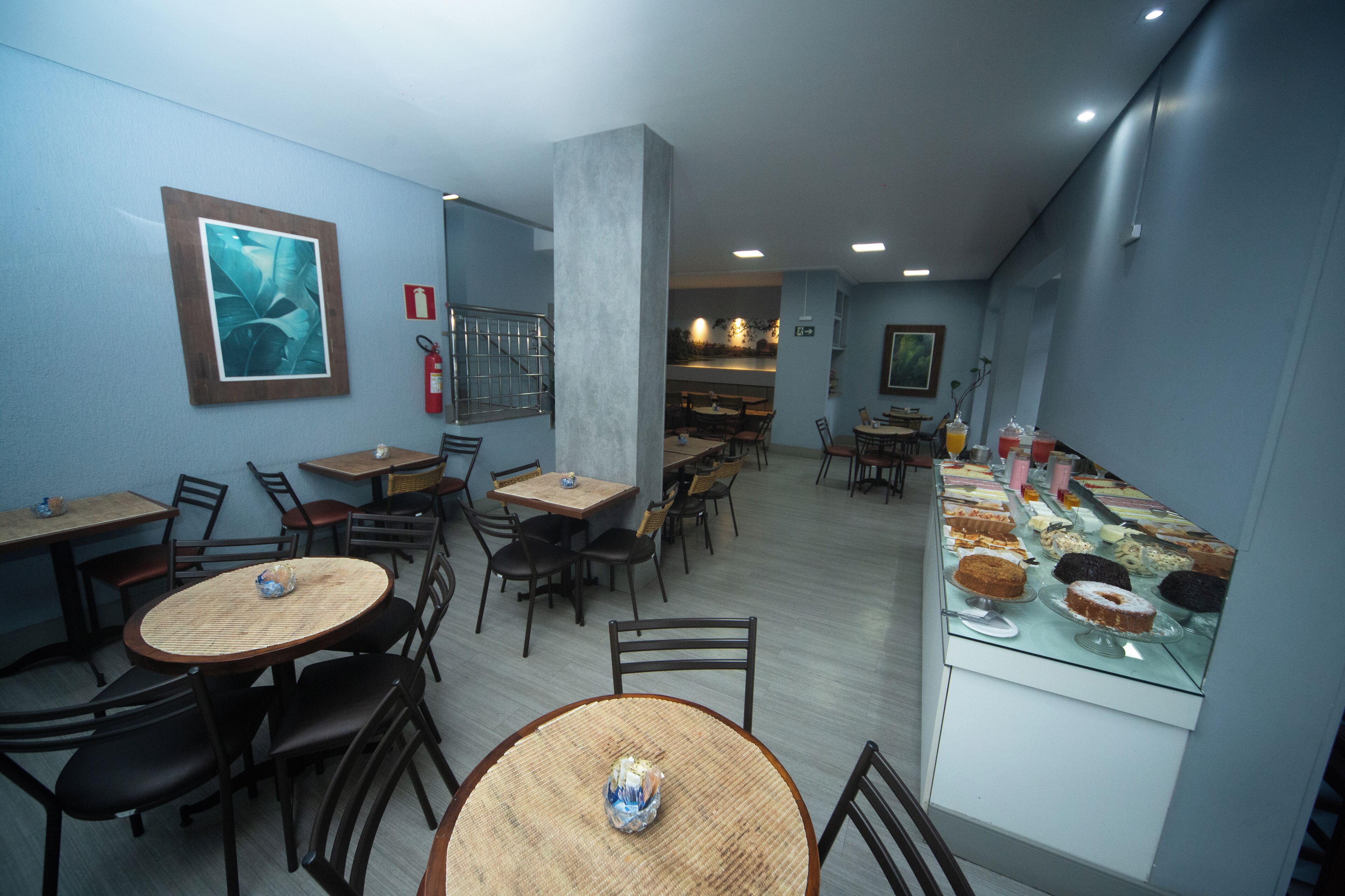 Un restaurante con mesas y sillas redondas, una vitrina con postres y un extintor en la pared.