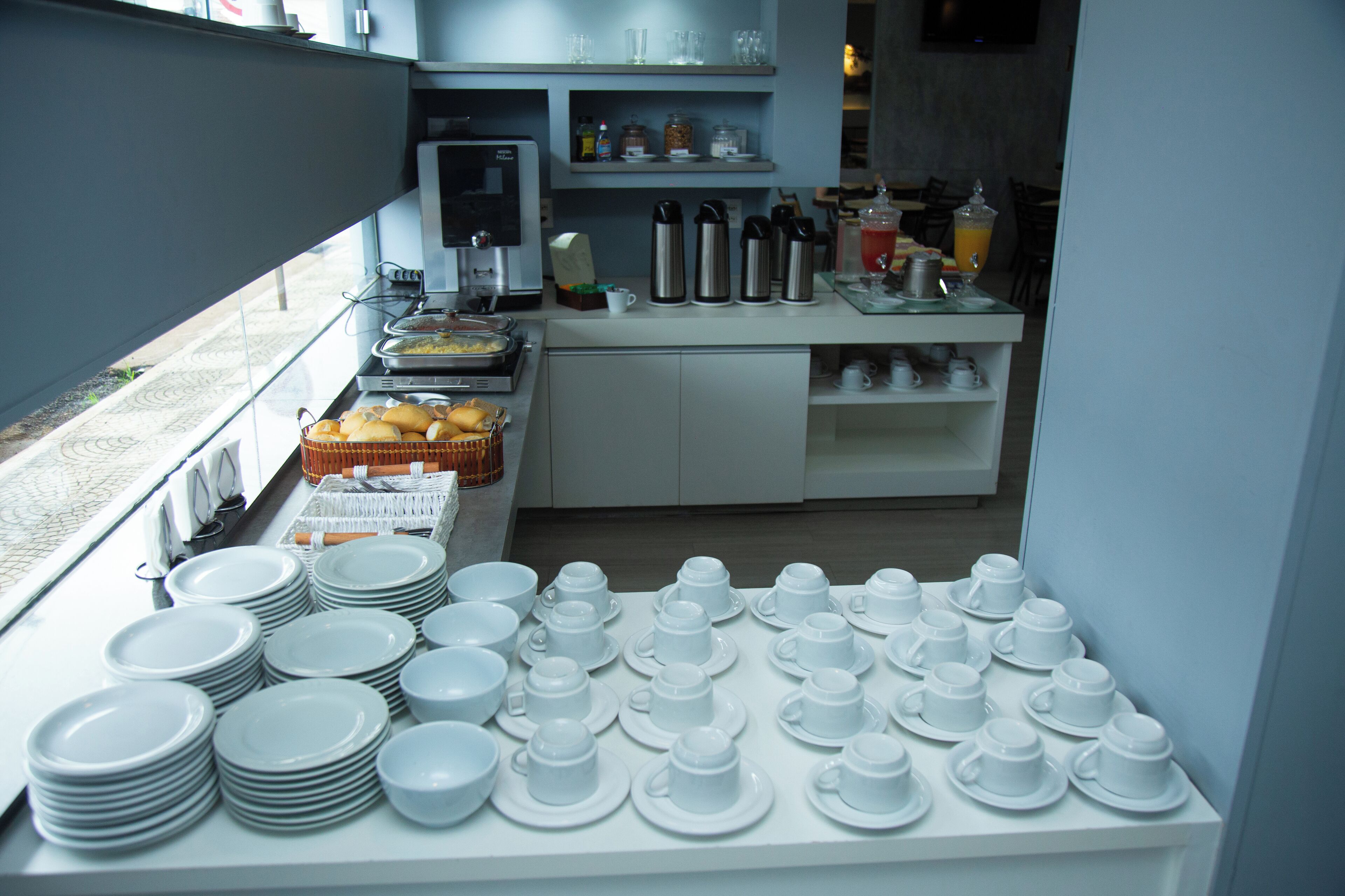 Un bufé de desayuno con diversos alimentos y una amplia selección de platos y tazas blancas.