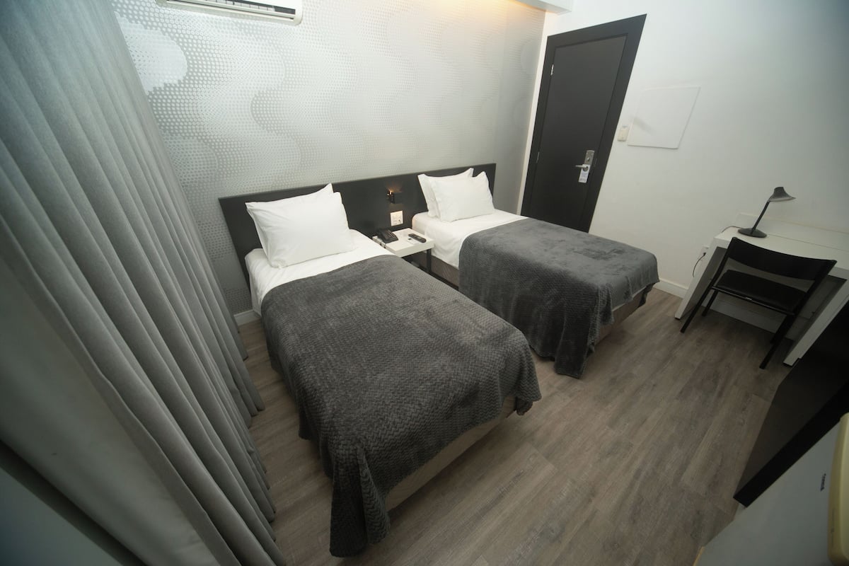 Quarto de hotel com duas camas, uma escrivaninha e uma cadeira.