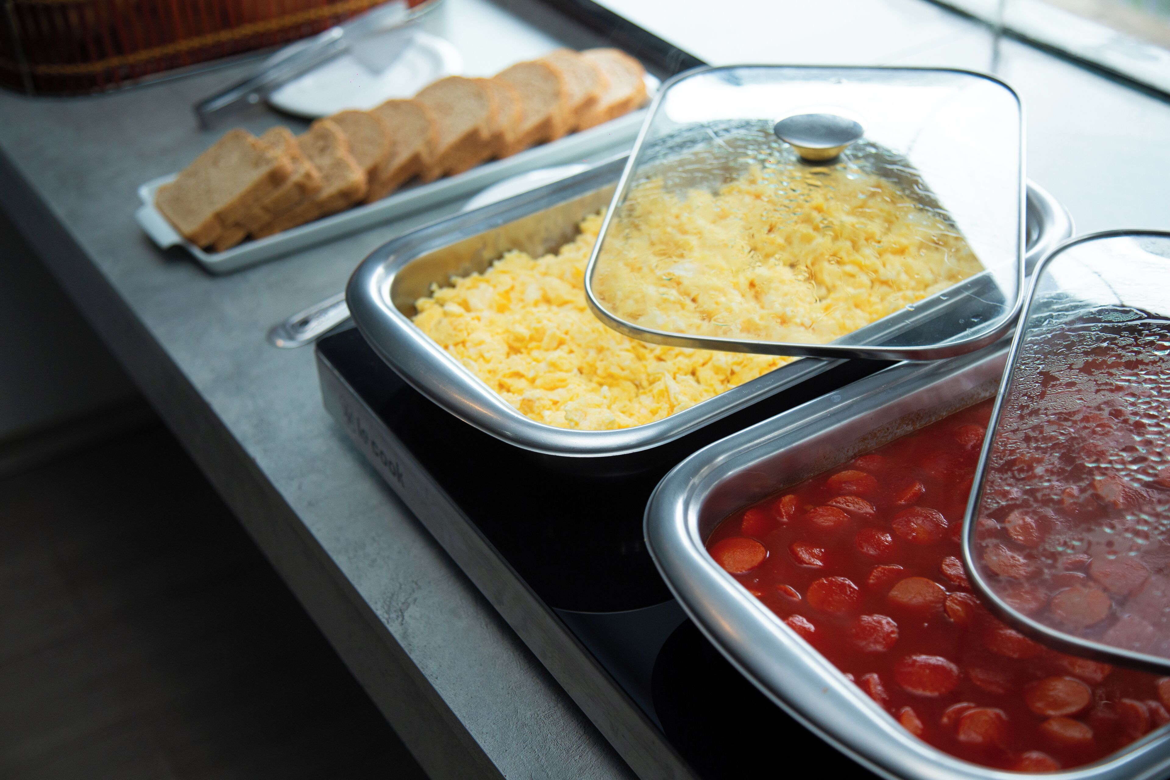 A buffet with trays of scrambled eggs, beans, and bread.