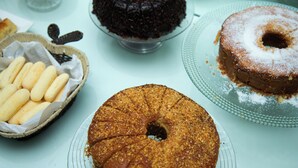 A table with various desserts including a bundt cake, a chocolate cake, and a cake with powdered sugar.