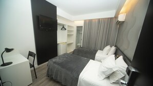 A modern hotel room with a bed, a desk, a chair, a TV, and a wardrobe.
