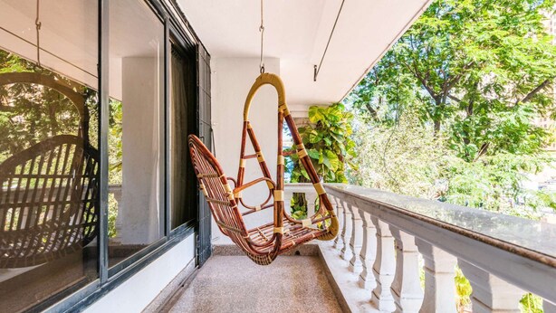 A balcony with a wicker chair, a white balustrade, and a view of greenery.