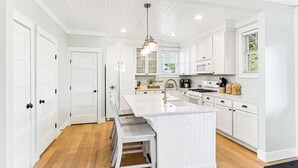 A modern kitchen with white cabinetry, a central island, and bar stools. - Seabrook's Someplace Else: Hot Tub, Pet Free, Steps From Town Center! (Pacific Beach)