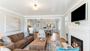 A spacious living room with a large sofa set, a coffee table, and a fireplace. There is a dining area in the background with a chandelier. - Seabrook's Someplace Else: Hot Tub, Pet Free, Steps From Town Center! (Pacific Beach)