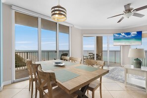 A dining area with a wooden table, chairs, and a view of the ocean through large sliding doors. - Sea Turtle Retreat! 817 END UNIT w/ Wrap Around Balcony and Panoramic Views! (Panama City Beach)