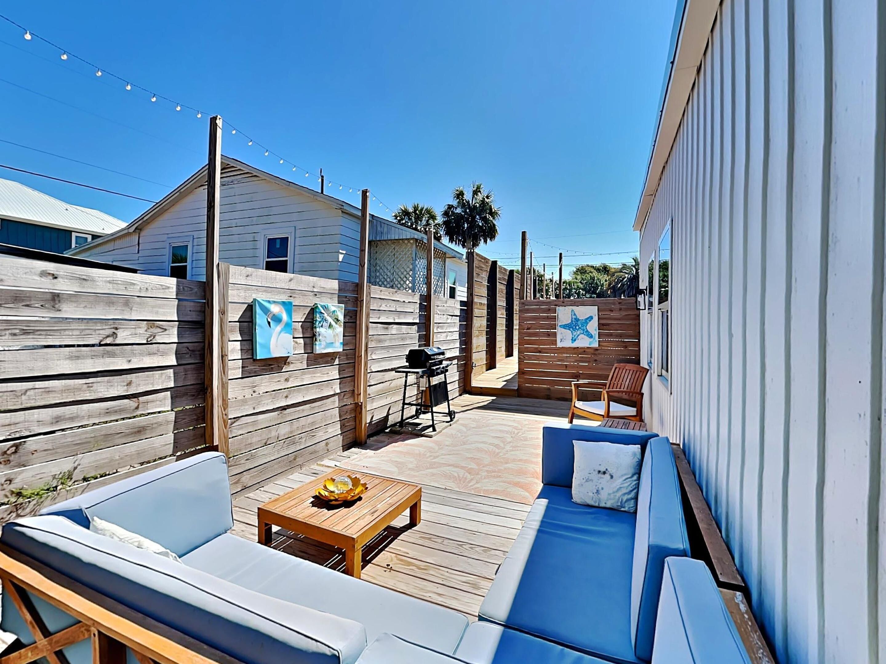 Un espace patio avec une terrasse en bois, un canapé bleu, une table en bois et un barbecue.