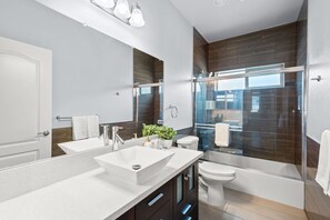 Een moderne badkamer met een grote spiegel, twee wasbakken, een toilet en een douchecabine met glazen wanden.