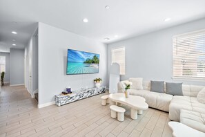 Een moderne woonkamer met een grote flatscreen-tv, een marmeren console tafel, een witte bank en een salontafel.