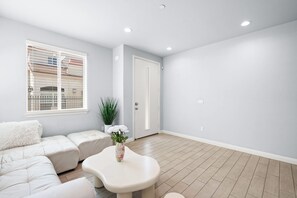 Een ruime woonkamer met een lichtgrijze bank, een witte salontafel en een potplant.