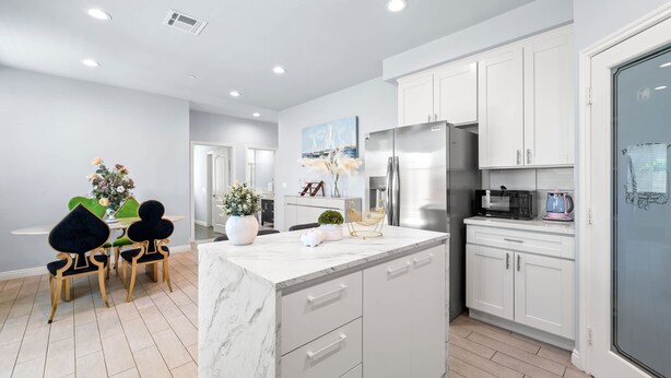 A modern kitchen with white cabinets, a marble island, and a dining area with a green table and black chairs. - Modern Spacious Home Bright Family Group Friendly (La Puente)