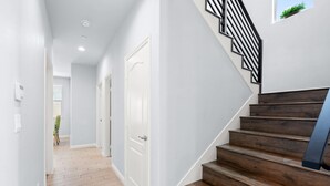 A hallway with wooden stairs and a white door. - Modern Spacious Home Bright Family Group Friendly (La Puente)