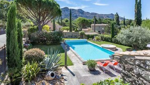 A swimming pool with a stone deck, surrounded by various plants and trees, with a mountainous backdrop. - La Villa de Robion in Robion (Robion)