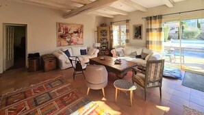 A spacious living area with a large sofa set, a coffee table, and a patterned rug. There is a painting on the wall and a view of the outdoors through a glass door. - La Villa de Robion in Robion (Robion)