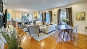 A modern living room with a sofa, coffee table, and dining area with chairs. - Cozy 5BR Jamaica Plain | Walk to T & Downtown (Boston)