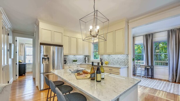 A modern kitchen with a central island, stainless steel appliances, and a geometric pendant light. - Cozy 5BR Jamaica Plain | Walk to T & Downtown (Boston)