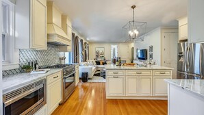 A modern kitchen with white cabinetry, stainless steel appliances, and a central island. - Cozy 5BR Jamaica Plain | Walk to T & Downtown (Boston)