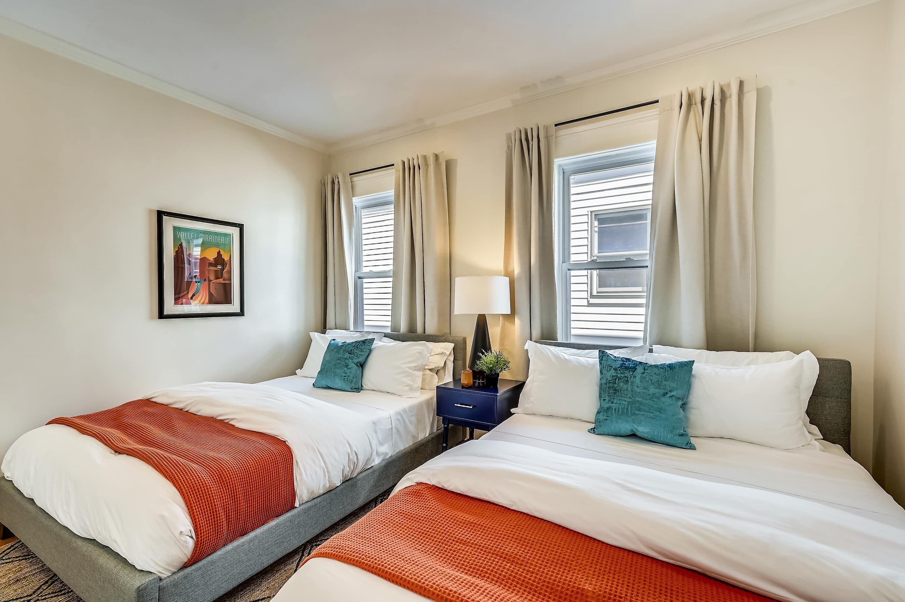 Une chambre d’hôtel avec deux lits, une table de chevet, une lampe et un tableau encadré au mur.