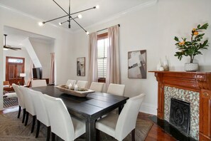 Un coin repas avec une table en bois foncé, des chaises blanches, un lustre, une cheminée et une plante en pot.