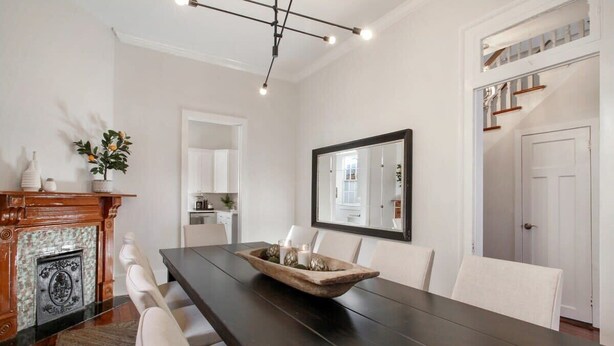 Une salle à manger avec une longue table en bois, des chaises blanches, une cheminée et un grand miroir au mur.