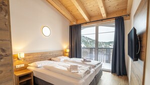 A bedroom with a wooden ceiling, a bed with white linens, a nightstand with a lamp, a TV mounted on the wall, and a balcony with curtains. - Spacious 4-bedroom Penthouse in Katschberghohe (Rennweg am Katschberg)