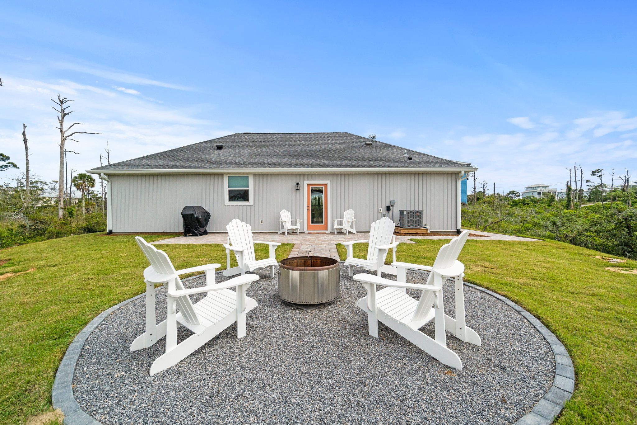 A house with a circular fire pit and four white Adirondack chairs in the front yard.