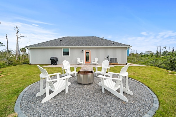 A house with a circular fire pit and four white Adirondack chairs in the front yard.