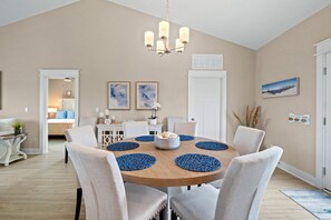 A dining area with a round table, beige walls, and a chandelier. There are two framed artworks on the wall and a door with a window.