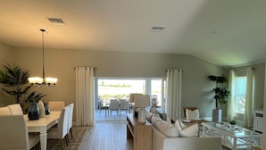 A spacious living room with a sofa, dining table, and chairs, a chandelier, and a view of the outdoors. - Stunning home with water view & golf cart Winter Cancellation - Reduced Rates (The Villages)