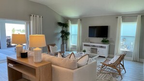 A modern living room with a sofa, coffee table, and lamps. There is a TV mounted on the wall and a plant in the corner. - Stunning home with water view & golf cart Winter Cancellation - Reduced Rates (The Villages)